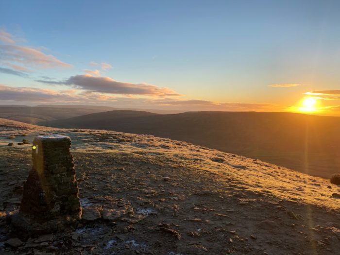 Sunrise across a hill showing the trigpoint in the foreground
