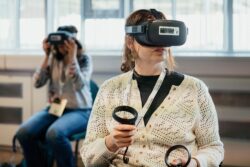 A seated student wears a VR headset and holds a VR controller in each hand.